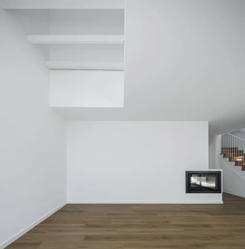Interior corner with white walls, timber flooring, floating shelves and recessed fireplace below suspended volumes