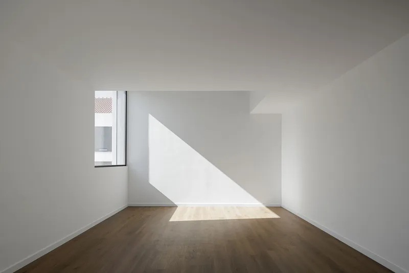 White room with timber floor and diagonal shaft of sunlight through corner window