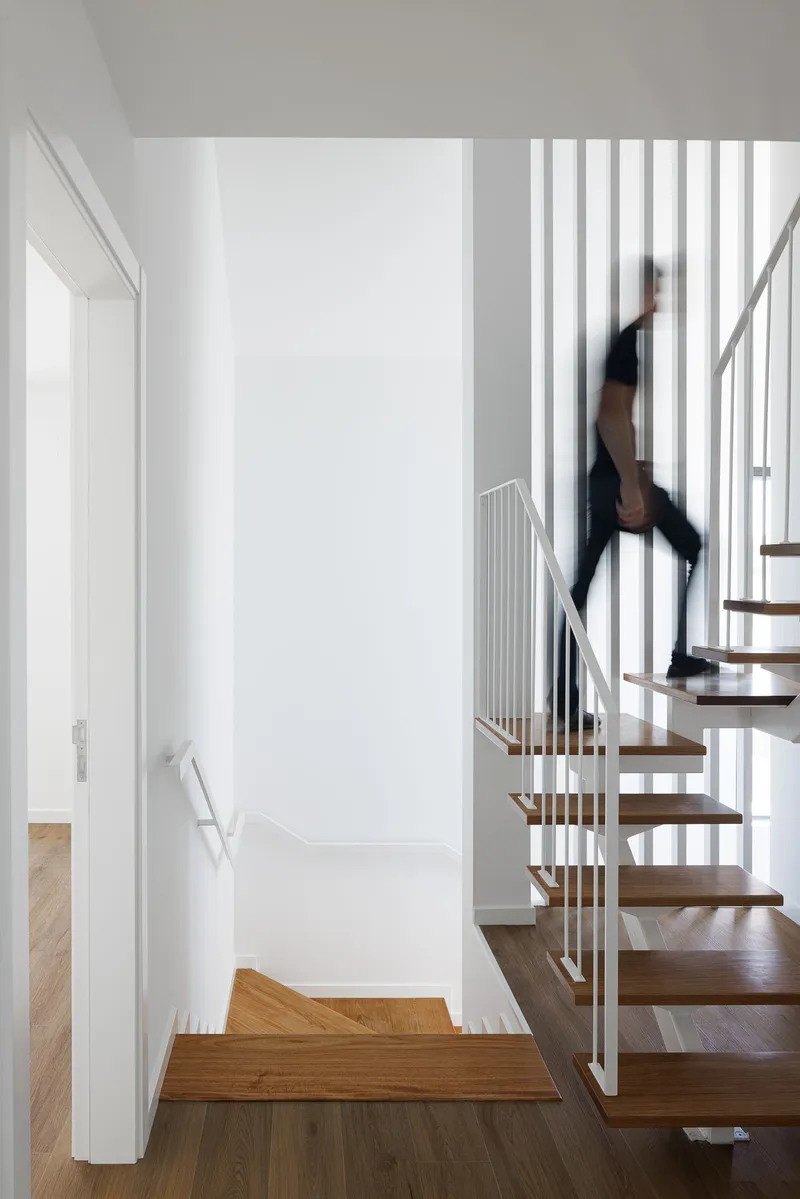 Open timber staircase with vertical white metal balusters and figure in motion ascending the treads