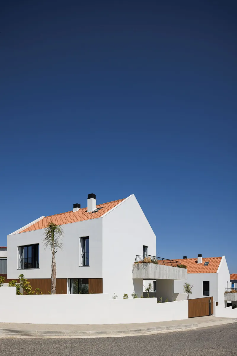 Street view of white plastered volumes with terracotta tile roofs and a palm tree under clear blue sky
