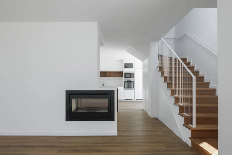 Open living space with timber staircase, vertical white balusters, and recessed black fireplace insert
