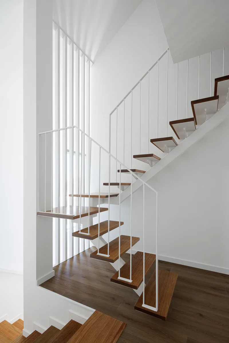 Open-tread staircase with timber treads and white steel frame between vertical balustrade panels
