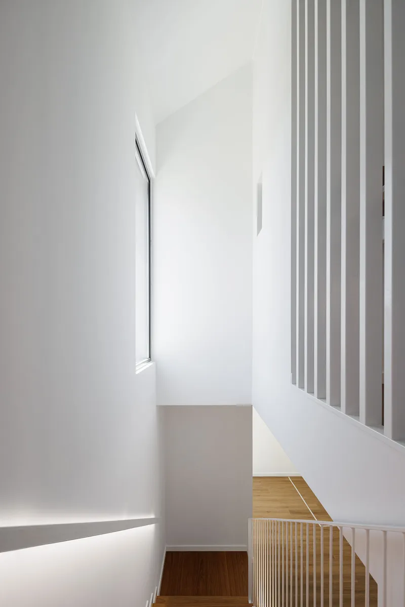 Upper hallway with narrow skylight, white walls, and vertical screen overlooking timber staircase below