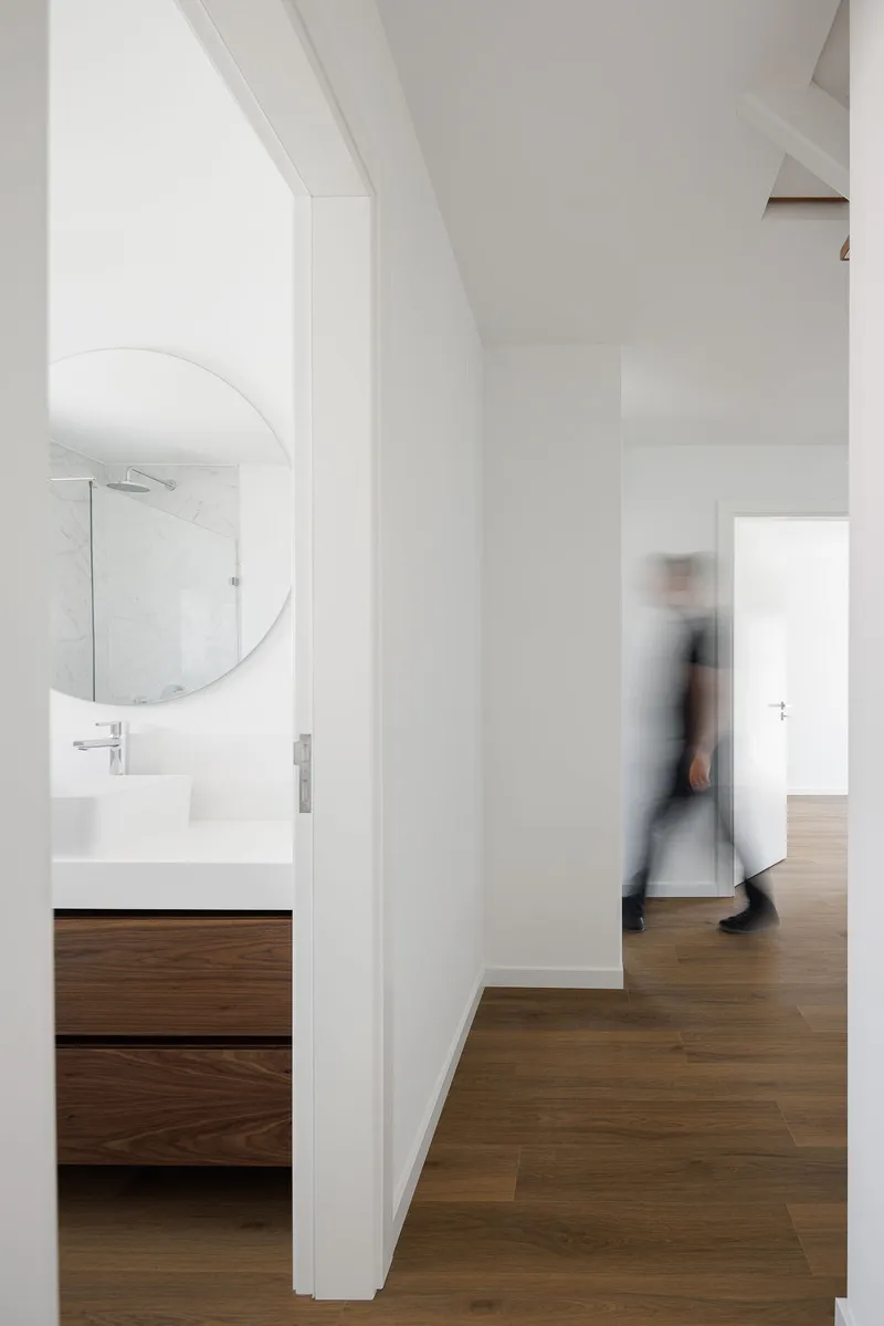 White corridor with walnut vanity base and a blurred figure walking past the bathroom entrance