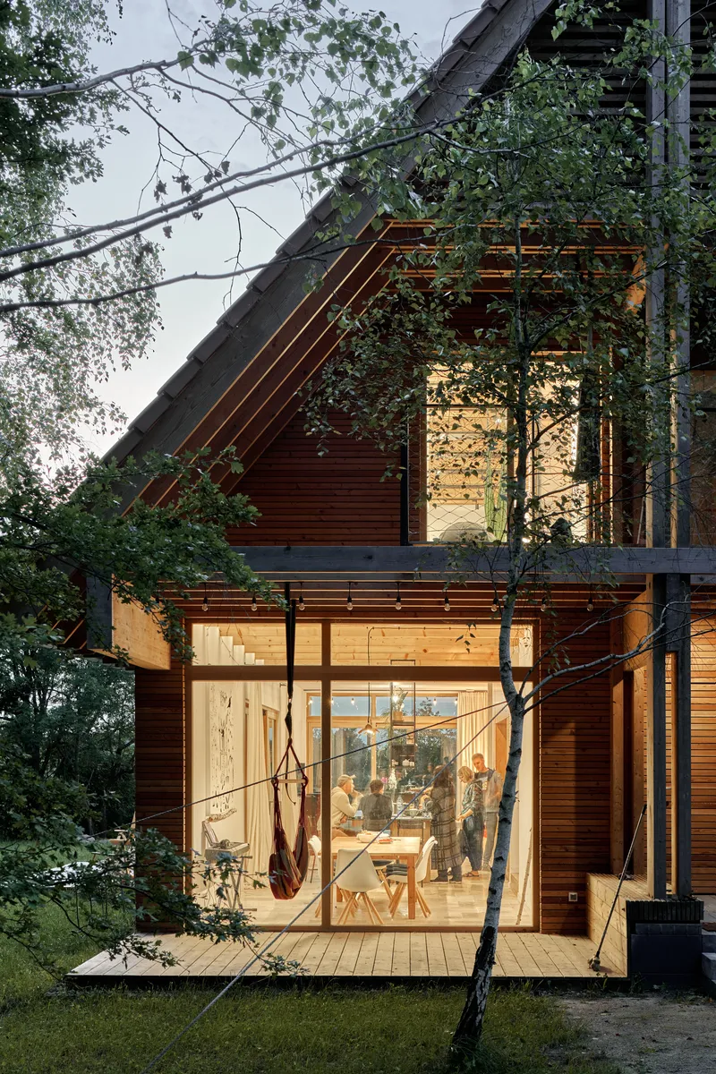 Glazed facade with horizontal wood cladding illuminated at dusk among birch trees and overhead wires