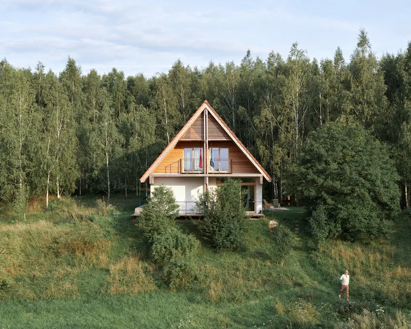 Two-story timber and plaster house with steep gabled roof nestled in a grassy meadow before a birch forest