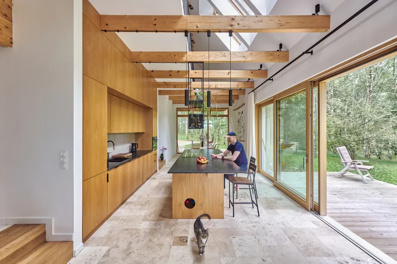 Open kitchen with wood cabinetry and exposed timber beams leading to sliding glass doors and terrace beyond
