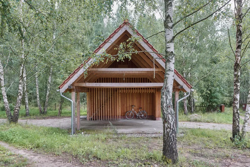 Open carport structure with vertical slat cladding and gabled roof framed by birch tree trunks