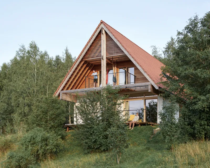 Two-story timber structure with steep red tile roof and exposed balcony framed by birch trees