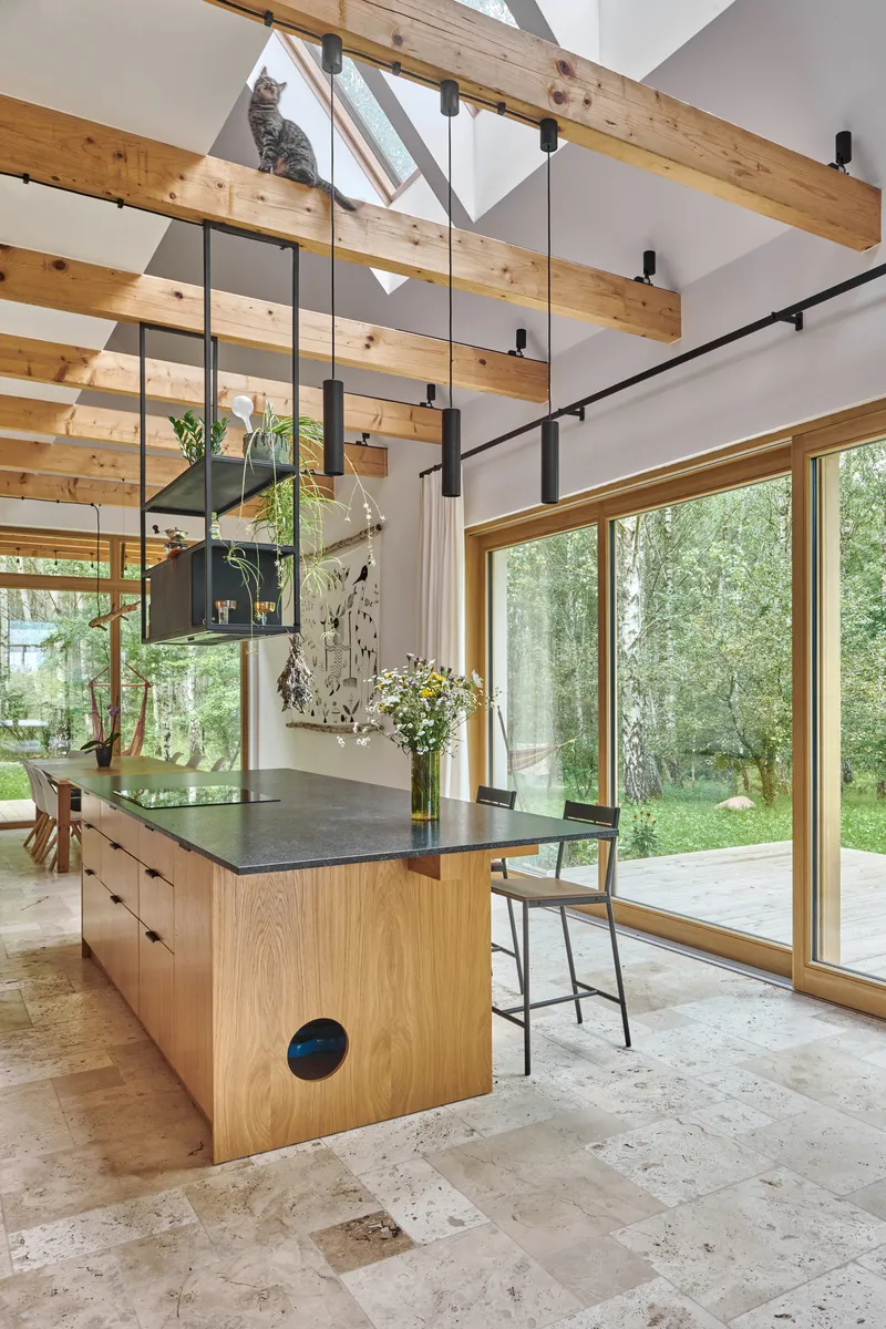 Double-height kitchen with oak island, exposed timber beams and glazed walls overlooking the forest