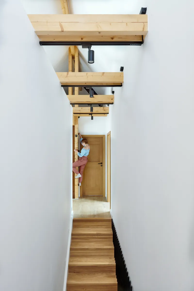 Vertical view up the timber stairwell with exposed beams and a figure pausing at the landing