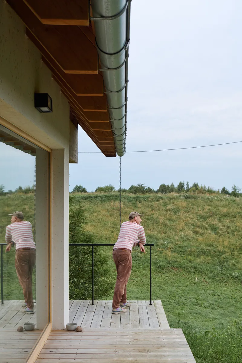 Timber deck balcony with metal ductwork at the eave and two figures overlooking a grassy slope