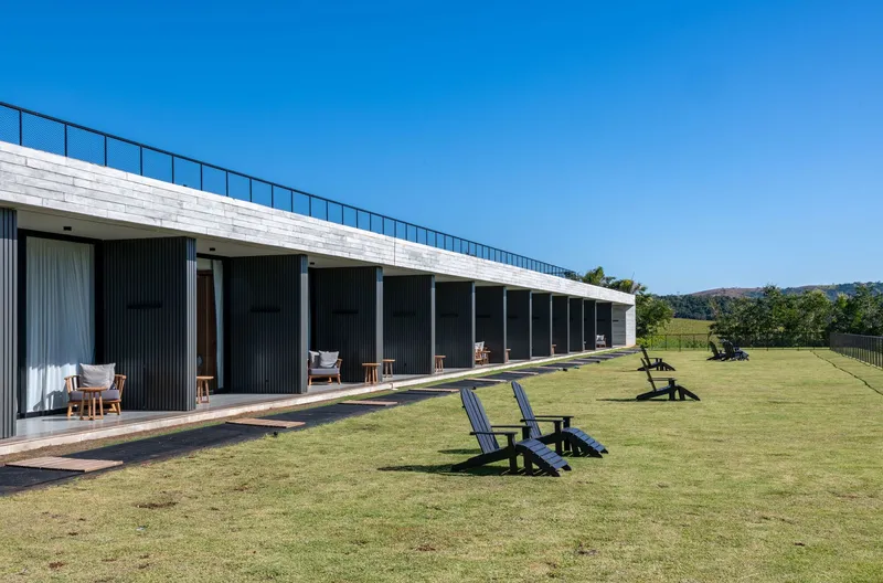Long facade with dark vertical cladding and continuous clerestory windows overlooking a grassy lawn with scattered chairs