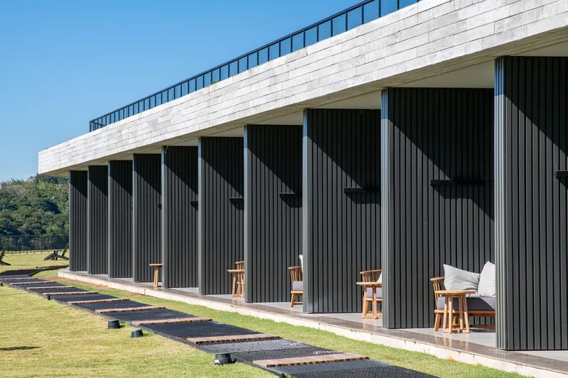 Repeating terrace openings framed by vertical dark cladding beneath a white horizontal roof parapet under clear sky