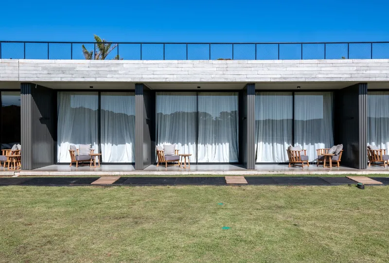 Series of glass doors with flowing white curtains opening onto individual timber-decked terraces facing a lawn