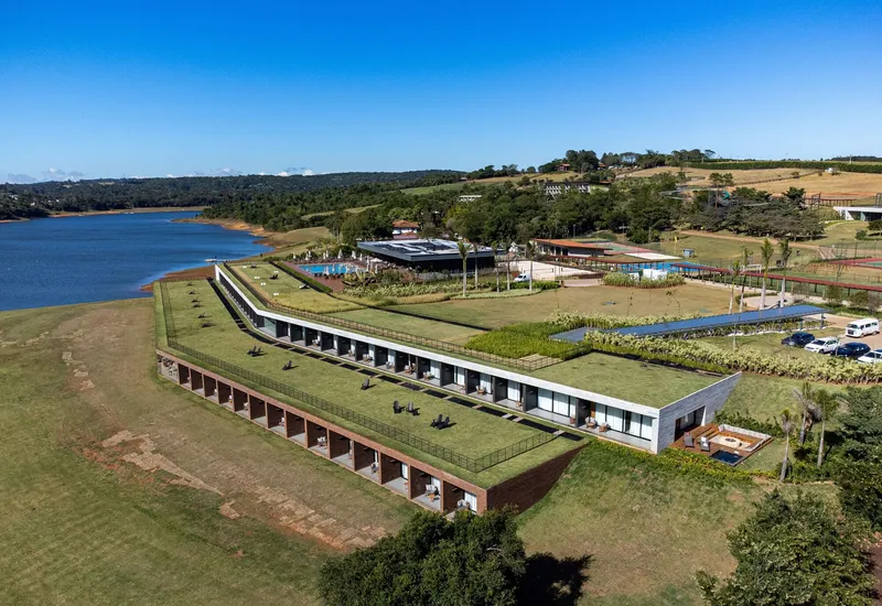 Aerial view of the green roof rising over a long facade with repeated brick openings beside a reservoir