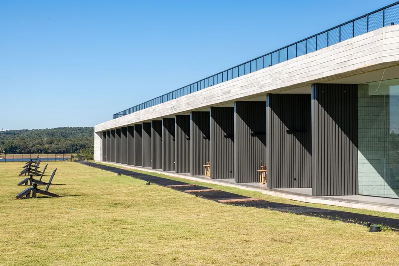 Facade with vertical timber battens below a white brick parapet and sloped green roof under clear sky