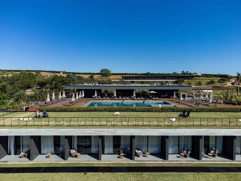 Terraced deck with pool loungers and planted hedges descending toward guest room balconies below green lawn
