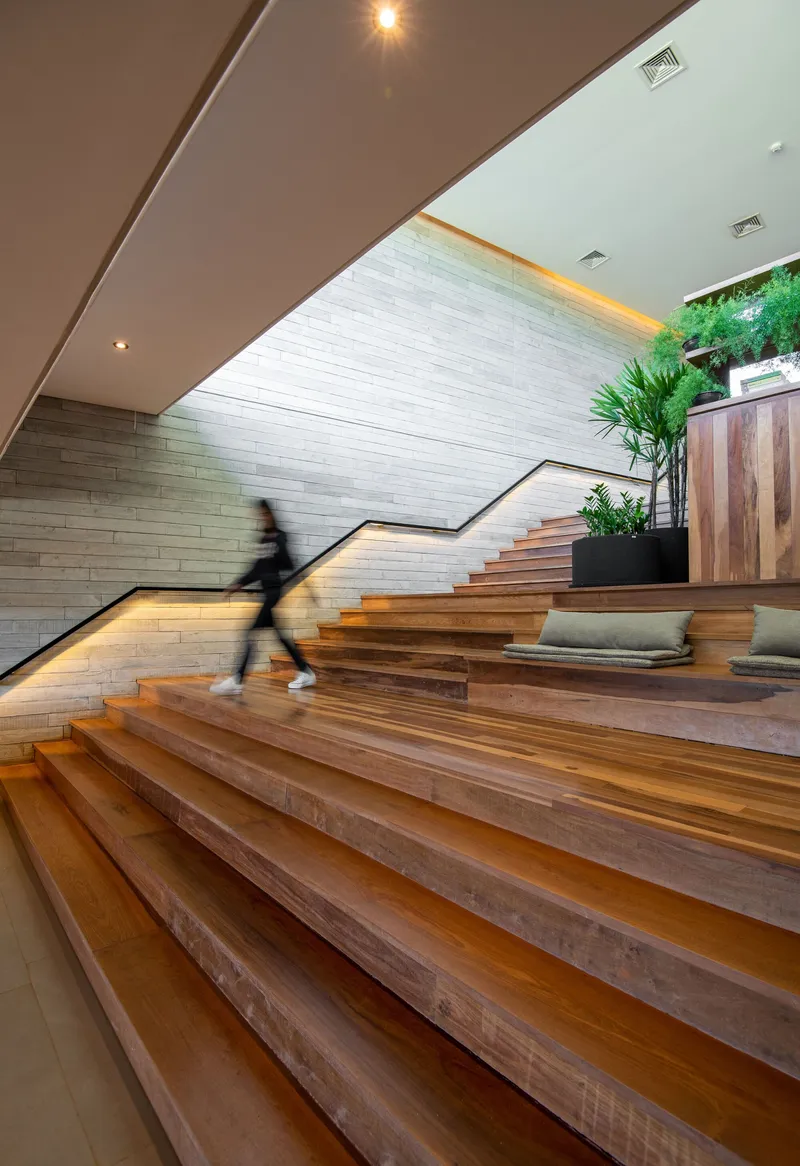 Wide timber staircase with metal handrail ascending through a white-painted brick lobby with a person in motion