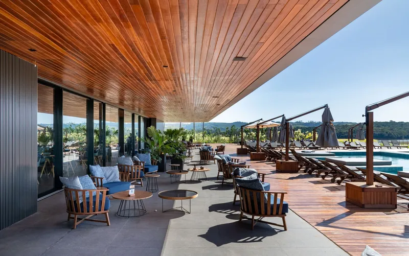 Covered terrace with slatted timber ceiling overlooking poolside lounge chairs and distant hills in afternoon light