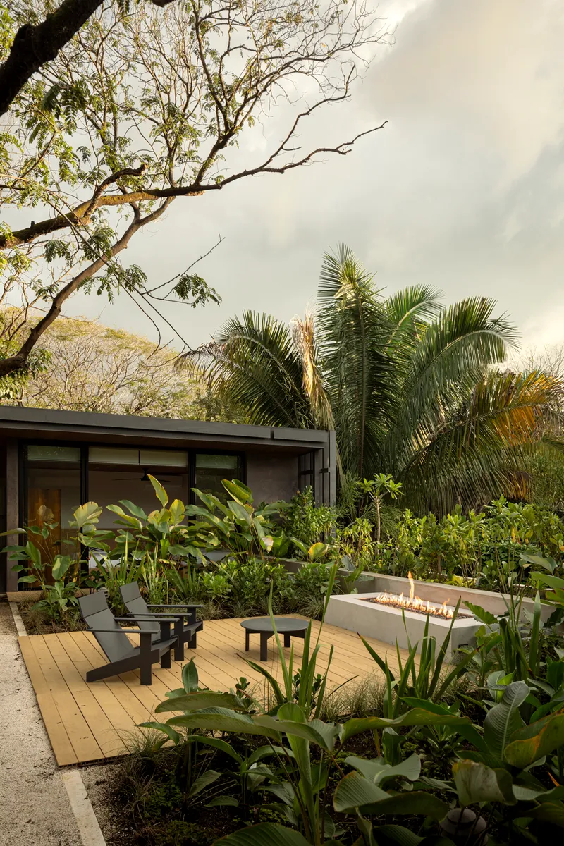Timber deck terrace with fire feature and lounge chairs amid planted beds under overcast sky