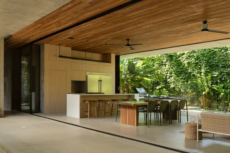 Covered outdoor kitchen and dining area with timber ceiling opening to planted garden wall