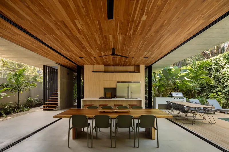 Dining area under timber ceiling with suspended staircase visible through planted courtyard opening
