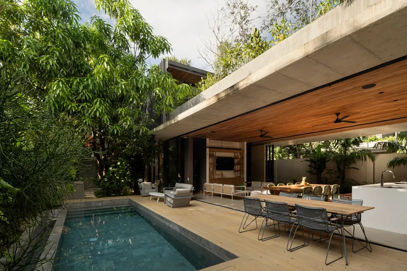 Outdoor dining area beside pool with cantilevered concrete roof and timber ceiling soffit