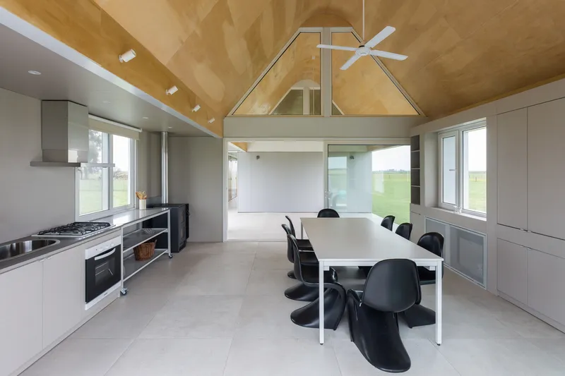 Open-plan kitchen and dining space with plywood vaulted ceiling and white cabinetry