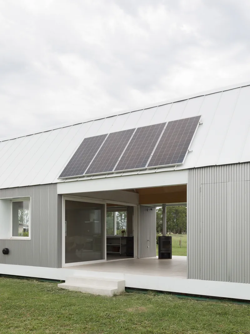 Concrete terrace and sliding doors beneath metal roof with four mounted solar panels