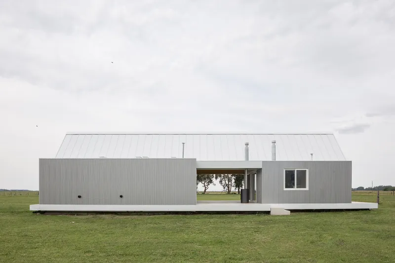 Long side elevation of corrugated metal volume on concrete plinth in grassy field