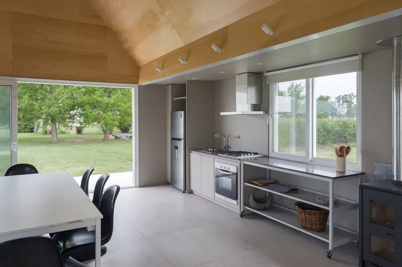 Open kitchen and dining area with plywood vaulted ceiling and floor-to-ceiling windows overlooking green lawn