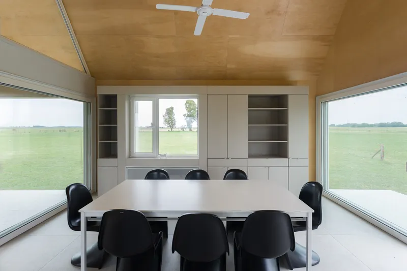Dining table with black chairs beneath plywood ceiling and built-in cabinetry with views to pasture