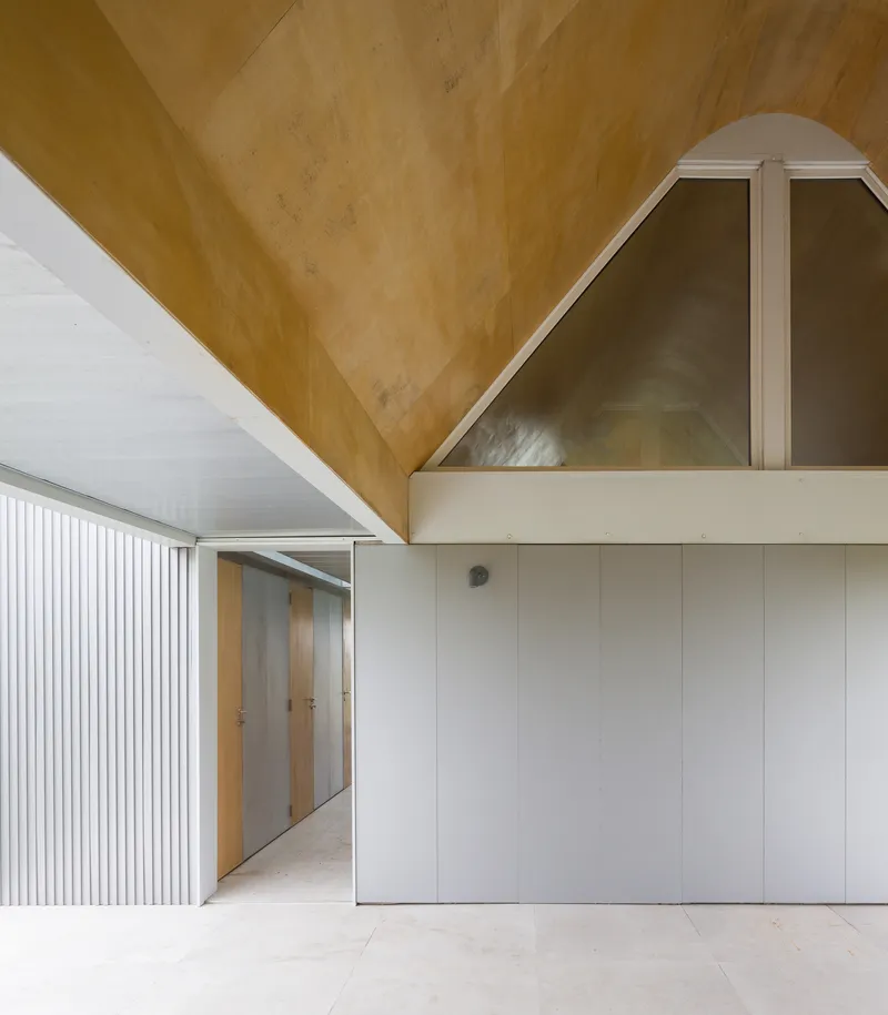 Interior hallway showing the intersection of plywood pitched ceiling and white-panelled storage volumes