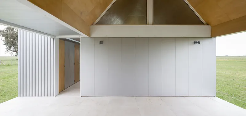 Covered entry terrace with white-panelled wall and corrugated metal cladding opening to green field