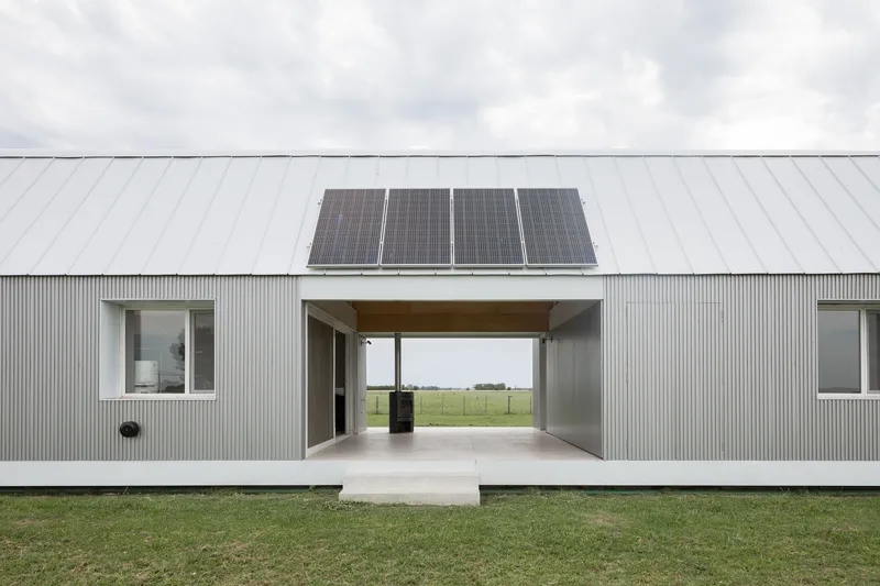 Corrugated metal facade with central breezeway passage and solar panels on the gabled roof