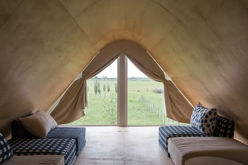 Interior view of plywood-lined gable ceiling with pointed window overlooking open farmland