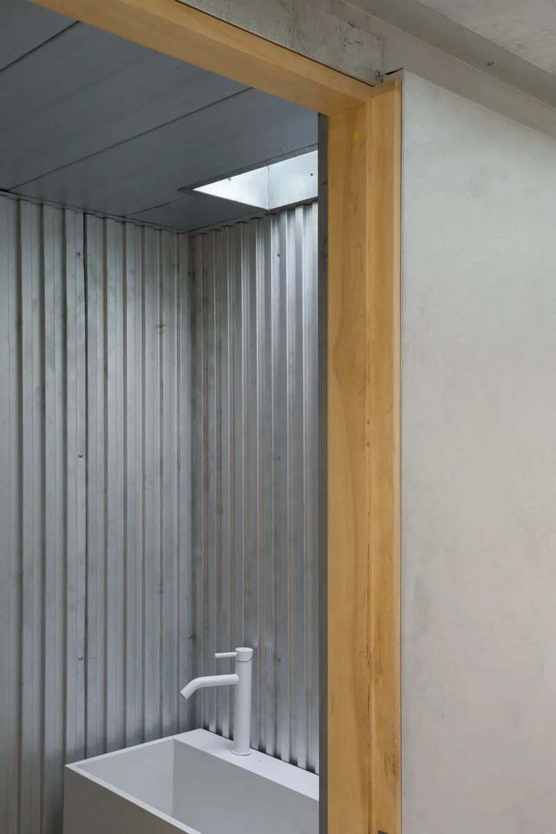 Bathroom niche with corrugated metal walls and timber frame under a grey ceiling with skylight