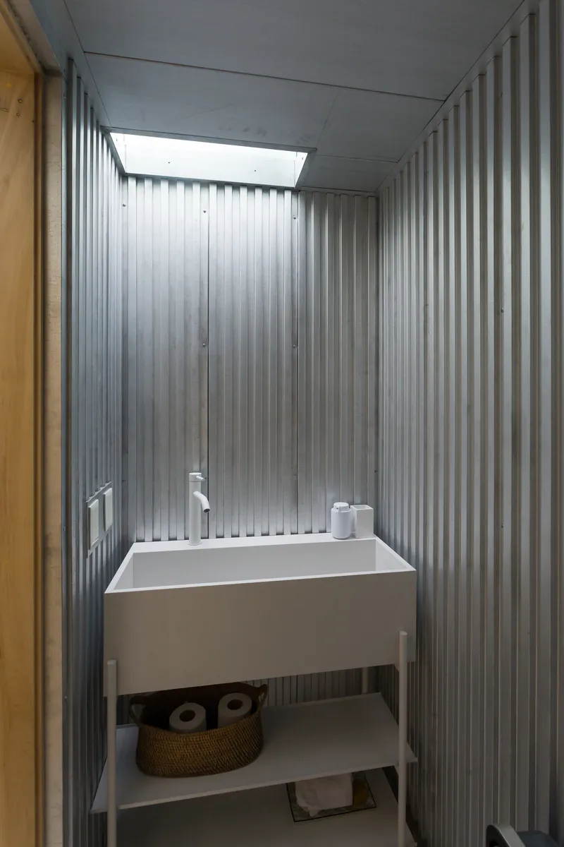 Small bathroom with white sink console and corrugated metal walls lit by a rectangular skylight