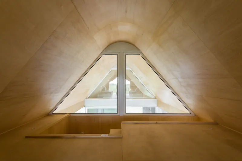 Arched triangular window set in a plywood-clad gable with a built-in bench below