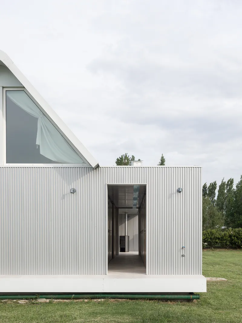 Vertical corrugated metal facade with a central doorway framing a view through to an interior corridor