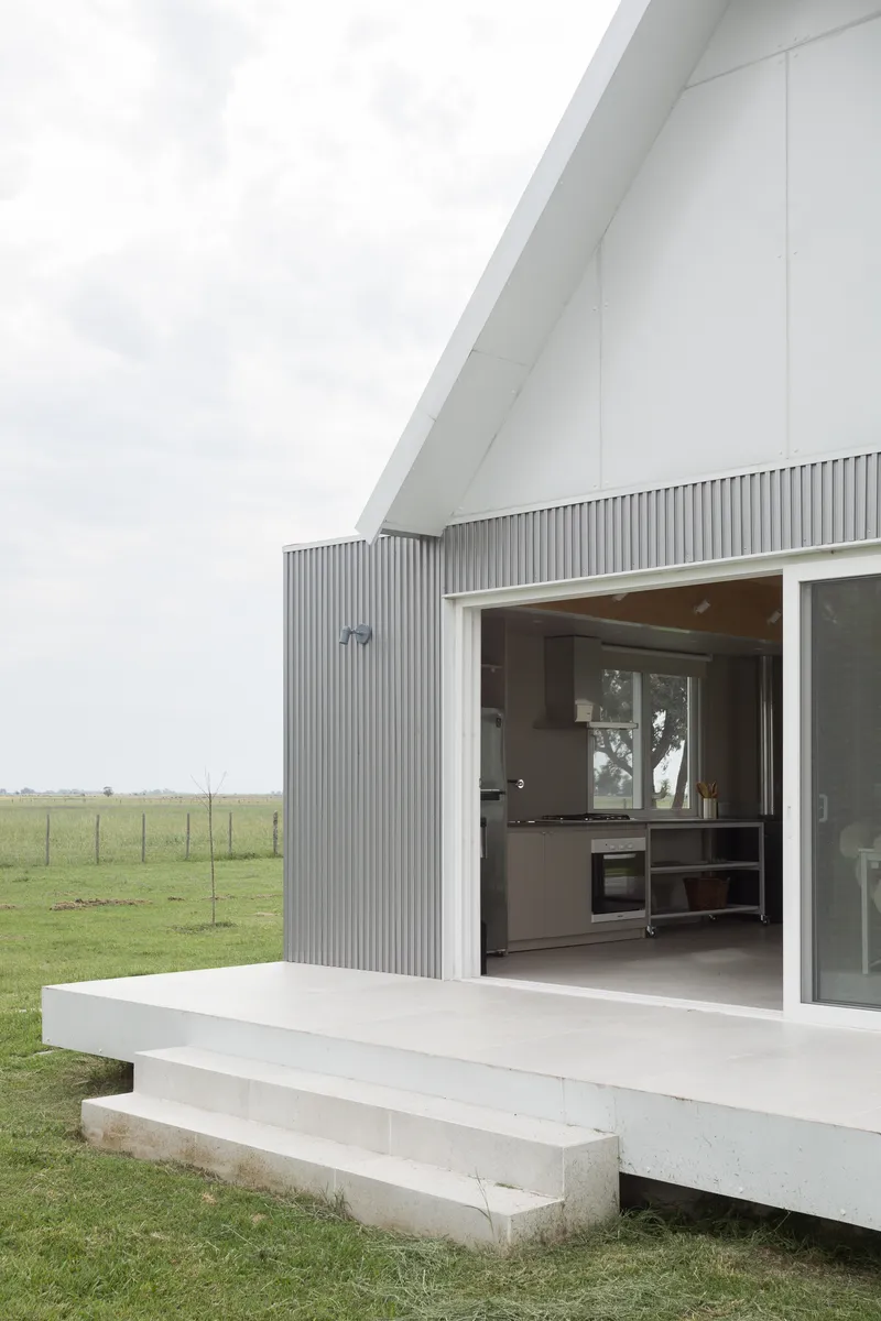 Open glass sliding doors revealing a kitchen inside, with a white terrace and concrete steps