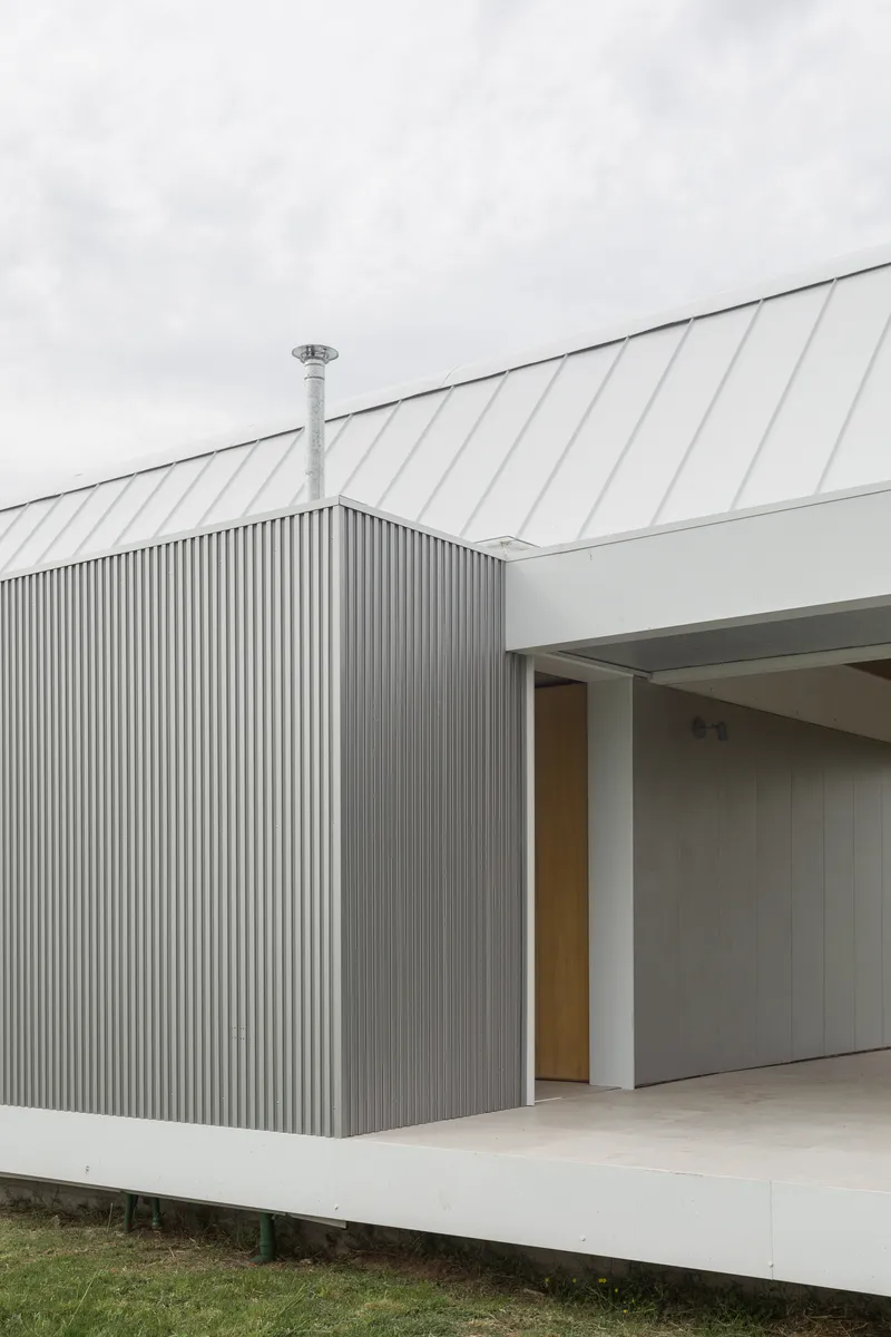 Detail of the corrugated metal wall meeting the sloped metal roof with a steel flue pipe