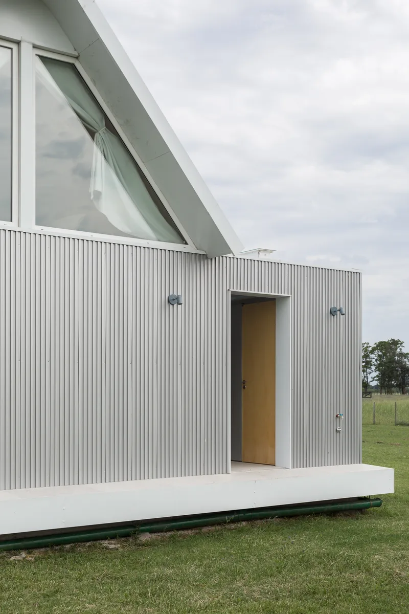 Facade view showing the angled glazed window above the corrugated metal volume on a raised terrace
