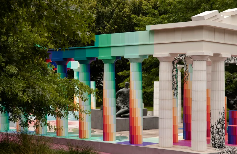 Close view through the colonnade showing gradient columns framing a sculptural element and trailing vines overhead