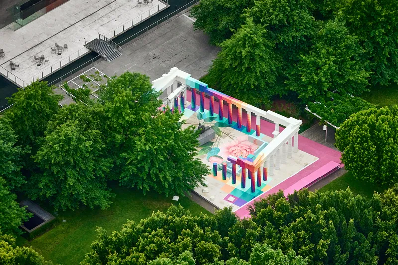 Aerial view of a colonnade with multicolored columns and painted floor murals surrounded by green trees