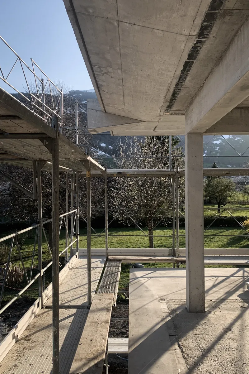 Underside of concrete slab with metal scaffolding and rectangular opening framing garden and trees beyond