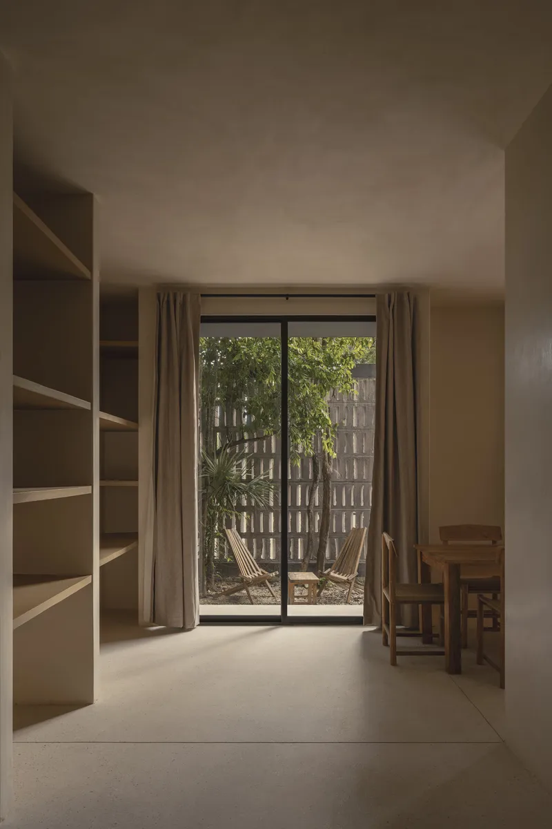 Interior room with built-in shelving and glazed doors opening to planted courtyard with block screen wall