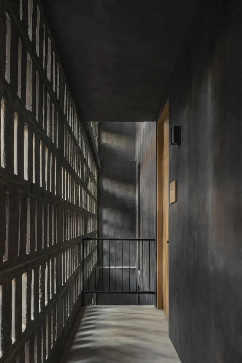 Interior corridor with perforated brick wall catching dramatic natural light beside a metal railing