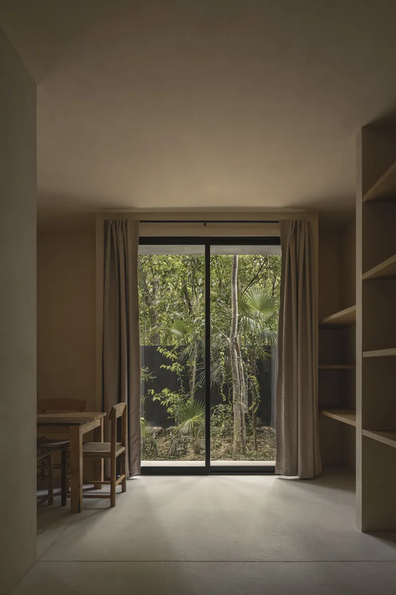 Living space with timber furniture opening to a glazed door framing dense garden vegetation beyond